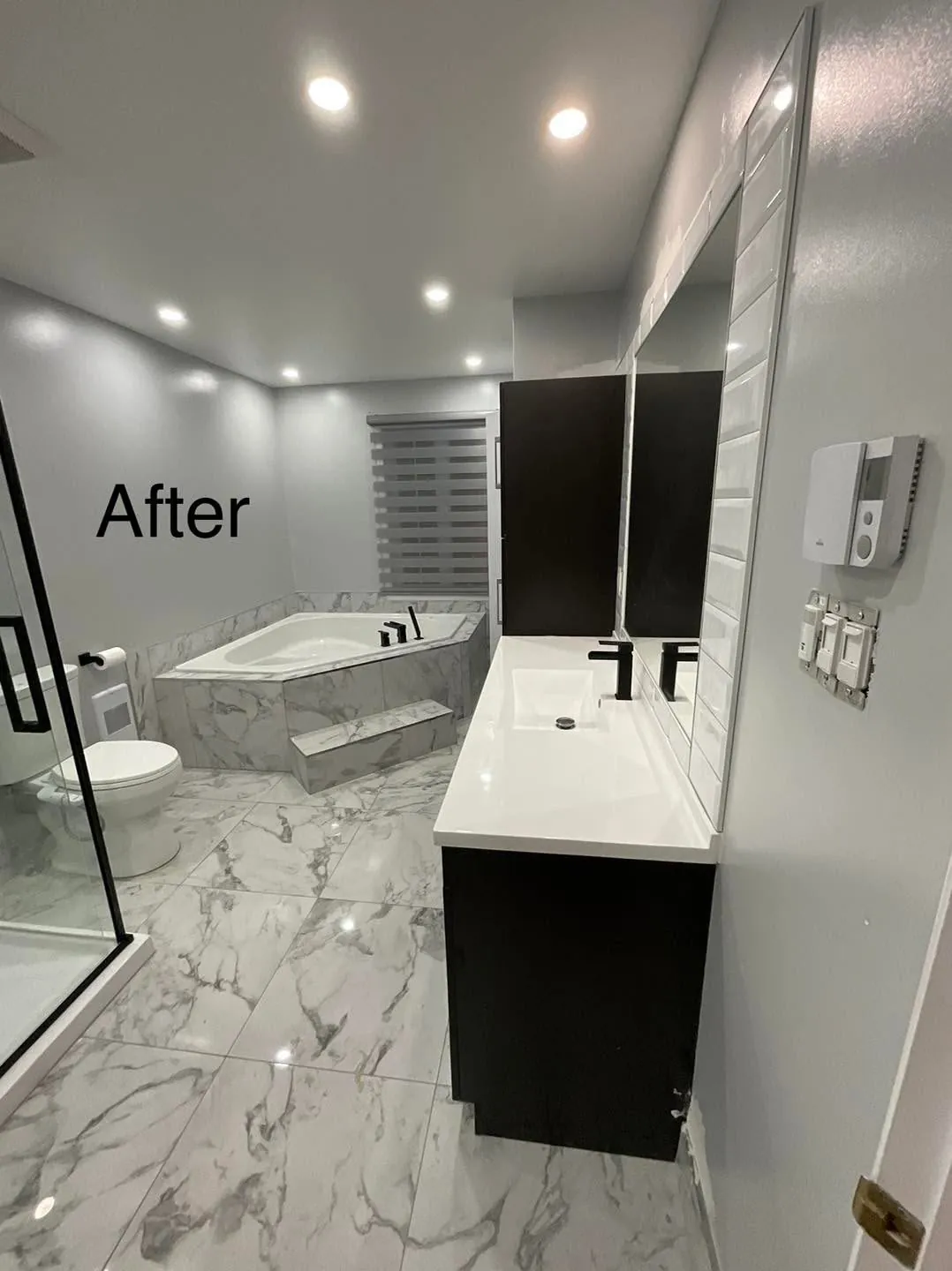 The same bathroom with marble look tile, a dark vanity and a tiled tub surround